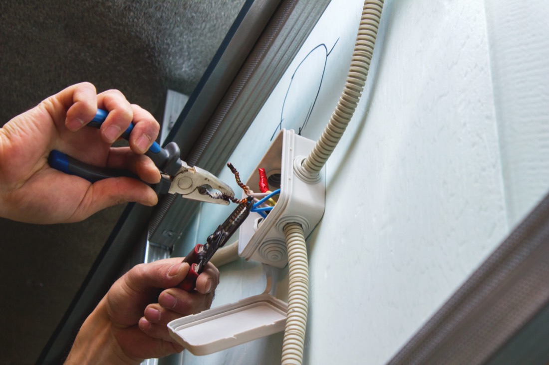 Hands using pliers on exposed wires in a wall-mounted electrical box