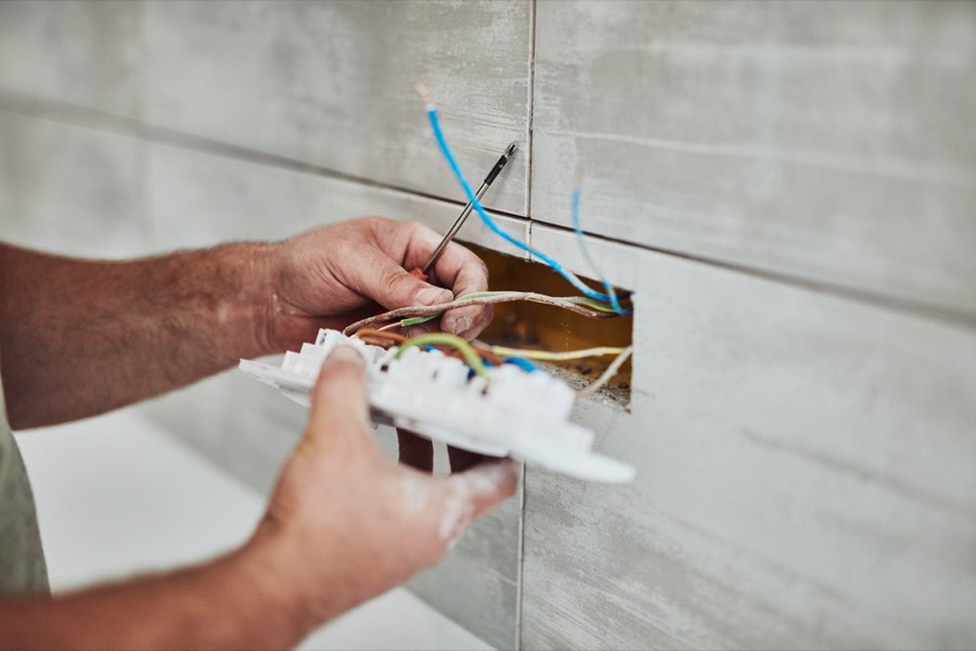 Electrician wiring a socket into a tiled wall