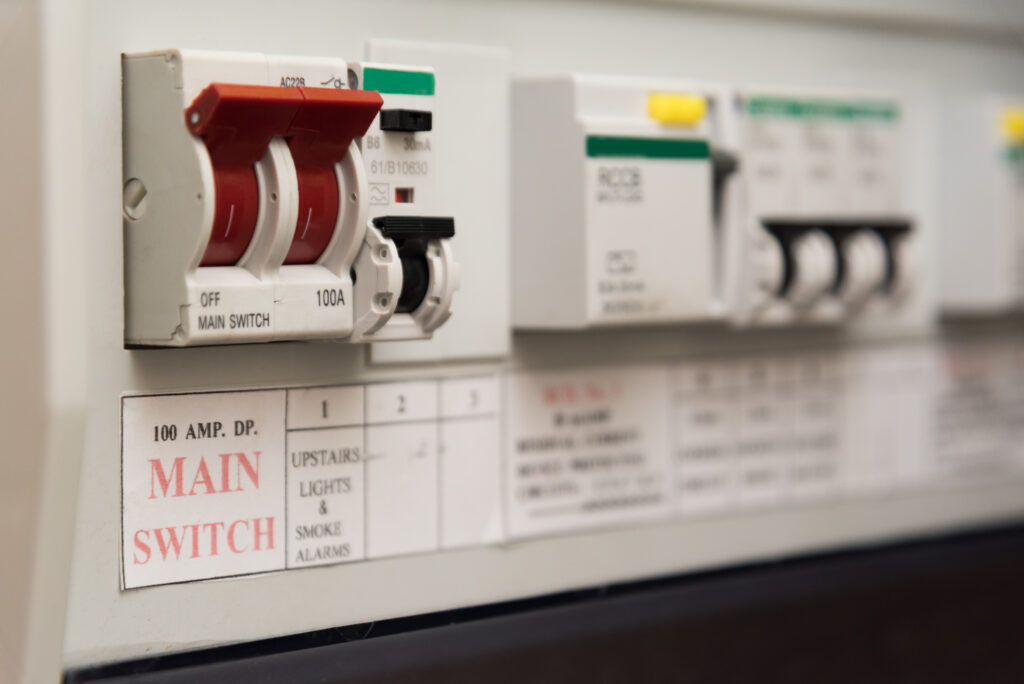 Close-up of an electrical panel with circuit breakers, including a prominent red switch labeled “MAIN SWITCH 100A” and other labeled switches for various household circuits.