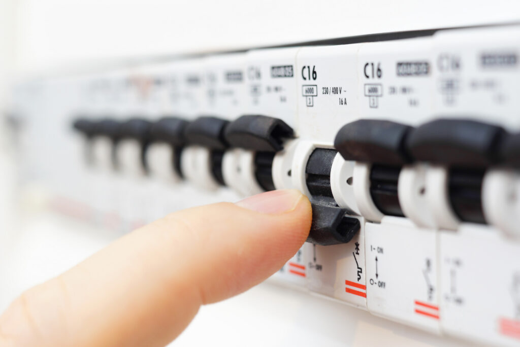 A close-up of a person’s finger flipping a switch on an electrical circuit breaker panel with several switches visible in a row.